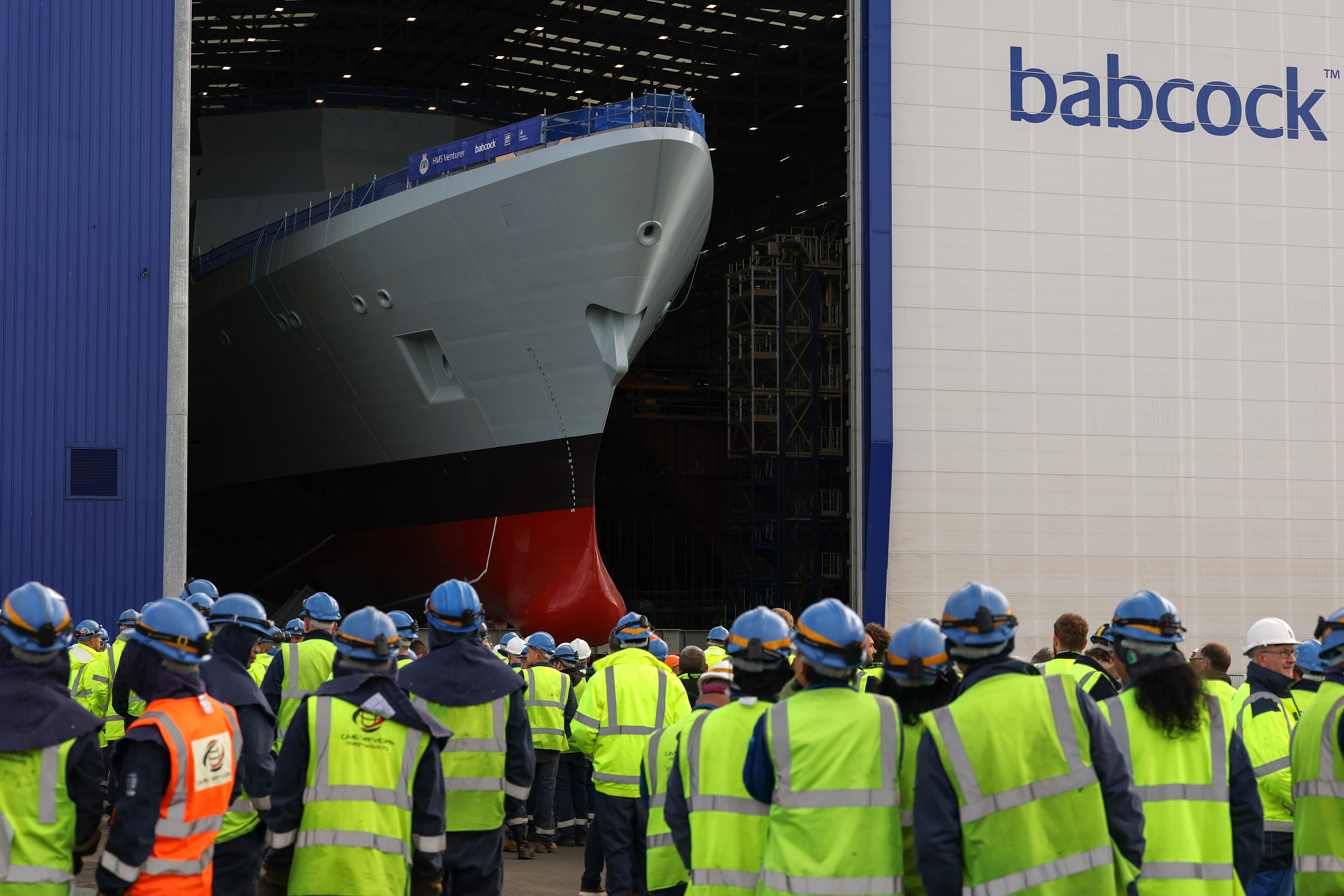 HMS Venturer, a Type 31 frigate, being rolled out of a building.